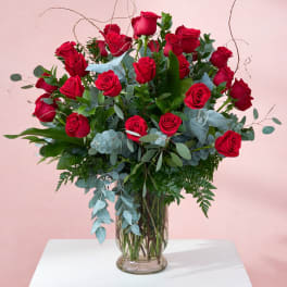 Red roses arranged in a clear glass vase with mixed greenery