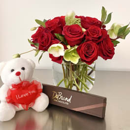 Red roses in a glass vase with a teddy bear and chocolate box