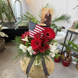 Red and white flower arrangement with an American flag and memorial card in a glass vase