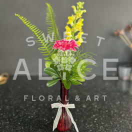 Pink and yellow flowers in a small red vase with a ribbon