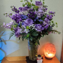 Purple floral arrangement in a glass vase on a small stand