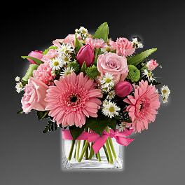Pink mixed flower bouquet in a clear glass vase with a ribbon