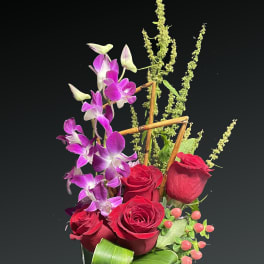 Red roses and purple orchids in a square glass vase