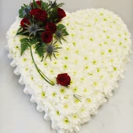 Heart-shaped white floral arrangement with red roses and greenery