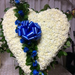 Heart-shaped white floral arrangement with blue roses and a blue ribbon