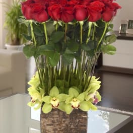 Tall arrangement of red roses with pale green orchids in a square glass vase
