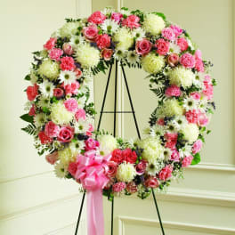 Pink and white floral wreath on a black stand with a pink ribbon