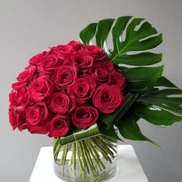 Bouquet of red roses with large tropical leaves in a clear glass vase