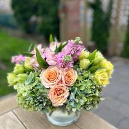Bouquet of peach roses, pink blooms, and green hydrangeas in a glass vase