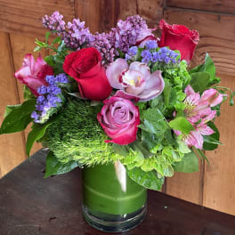 Mixed bouquet of roses, orchids, and purple filler flowers in a glass vase
