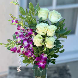 White roses and purple orchids arranged in a clear glass vase