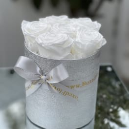 White roses arranged in a silver round box with a satin bow