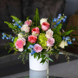 Arrangement of pink and cream roses with blue blooms in a white vase