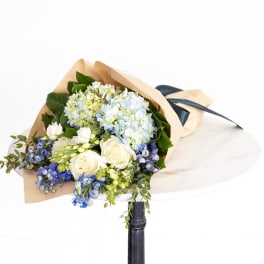 Bouquet of blue hydrangeas, white roses, and blue flowers wrapped in paper