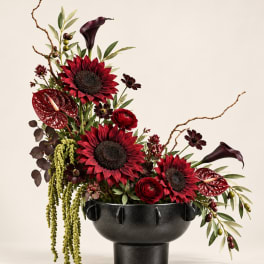 Red and burgundy floral arrangement in a black pedestal vase