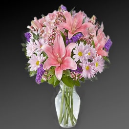 Pink lilies and daisies arranged in a clear glass vase