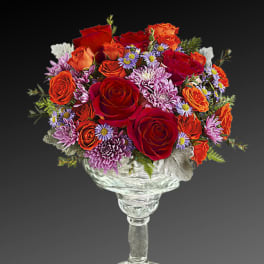 Mixed bouquet of red and orange roses with purple daisies in a clear glass vase