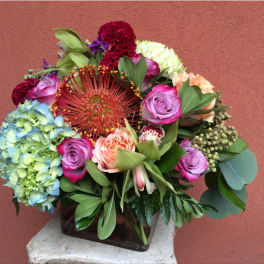 Mixed bouquet with roses, hydrangea, and a large red pincushion bloom in a square vase