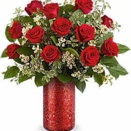 Red roses arranged in a red vase with white filler flowers
