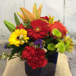 Colorful mixed bouquet in a dark blue vase with gerbera daisies, lilies, and carnations