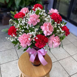 Pink and red carnations in a glass vase with a pink ribbon