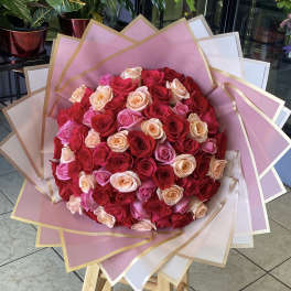 Large bouquet of red, pink, and peach roses wrapped in pink paper