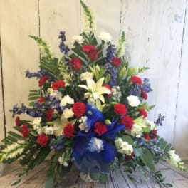 Large floral spray with red, white, and blue flowers in a blue ribbon wrap