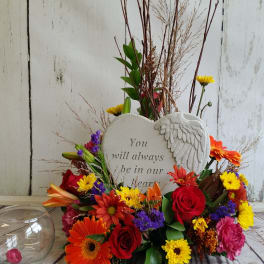 Heart-shaped memorial plaque surrounded by colorful flowers and a glass candle holder