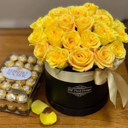 Yellow roses in a black hatbox beside a box of Ferrero Rocher chocolates