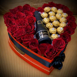 Heart-shaped box with red roses, gold chocolates, and a champagne bottle