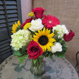 Mixed bouquet of roses, sunflowers, gerbera daisies, and hydrangeas in a glass vase