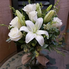 Arrangement of white lilies and roses in a clear glass vase with a burlap bow.