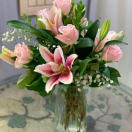 Pink roses and pink-and-white lilies arranged in a clear glass vase