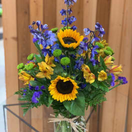 Bouquet of sunflowers, blue flowers, and yellow alstroemeria in a glass vase