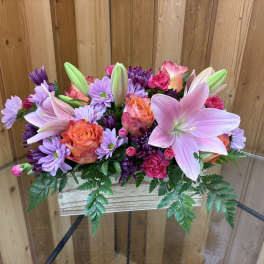 Low arrangement of pink lilies, orange roses, and purple mums in a rustic wooden box