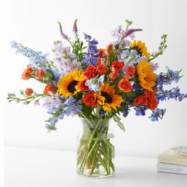 Mixed bouquet of sunflowers, roses, and blue flowers in a glass vase