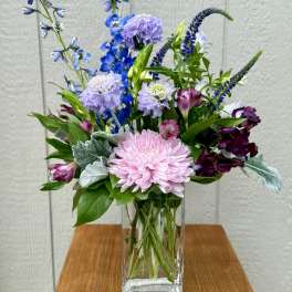 Mixed bouquet of pink, purple, and blue flowers in a clear glass vase