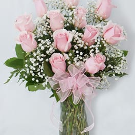 Pink roses in a glass vase with baby's breath and a pink ribbon
