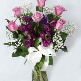 Pink roses and purple flowers in a glass vase with a white ribbon