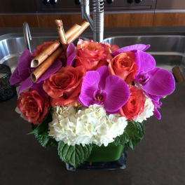 Bouquet of orange roses, purple orchids, and white hydrangeas in a square vase