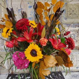 Autumn bouquet with sunflowers, red lilies, and orange leaves in a glass vase