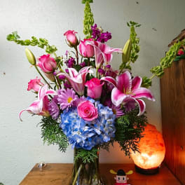 Pink lilies and roses with blue hydrangea in a glass vase