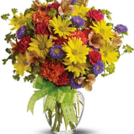 Mixed bouquet of yellow, red, and purple flowers in a glass vase with a green ribbon