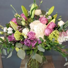 Tall mixed bouquet of pink roses, white hydrangeas, and lilies in a clear glass vase