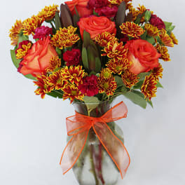 Bouquet of orange roses and red chrysanthemums in a glass vase with an orange ribbon
