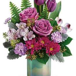 Purple roses and tulips in a glass vase with mixed pink flowers