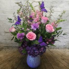Pink roses and purple flowers in a textured vase with butterfly picks