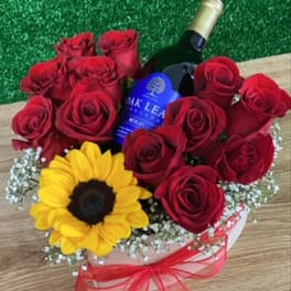 Red roses and a sunflower arranged around a wine bottle in a gift box