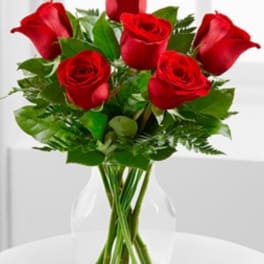 Medium bouquet of red roses arranged with foliage in a clear glass vase