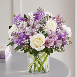 Bouquet of white roses and purple flowers in a clear glass vase